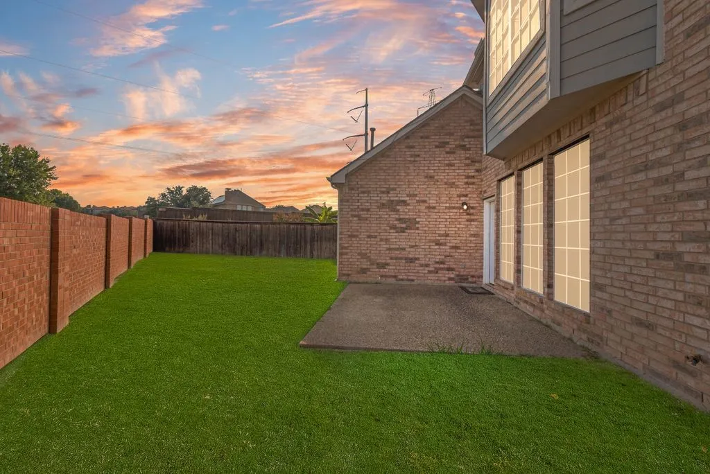 Expansive green lawn, brick perimeter fencing, concrete patio, and a two-story brick exterior with large windows