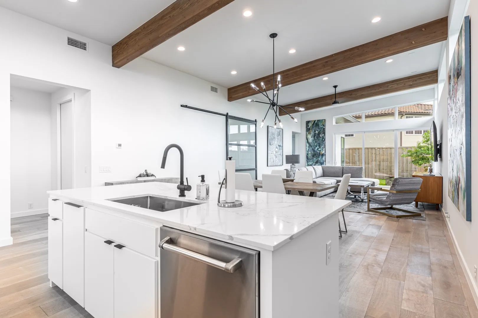 Kitchen with stainless steel dishwasher, beam ceiling, a barn door, an island with sink, and light wood finished floors