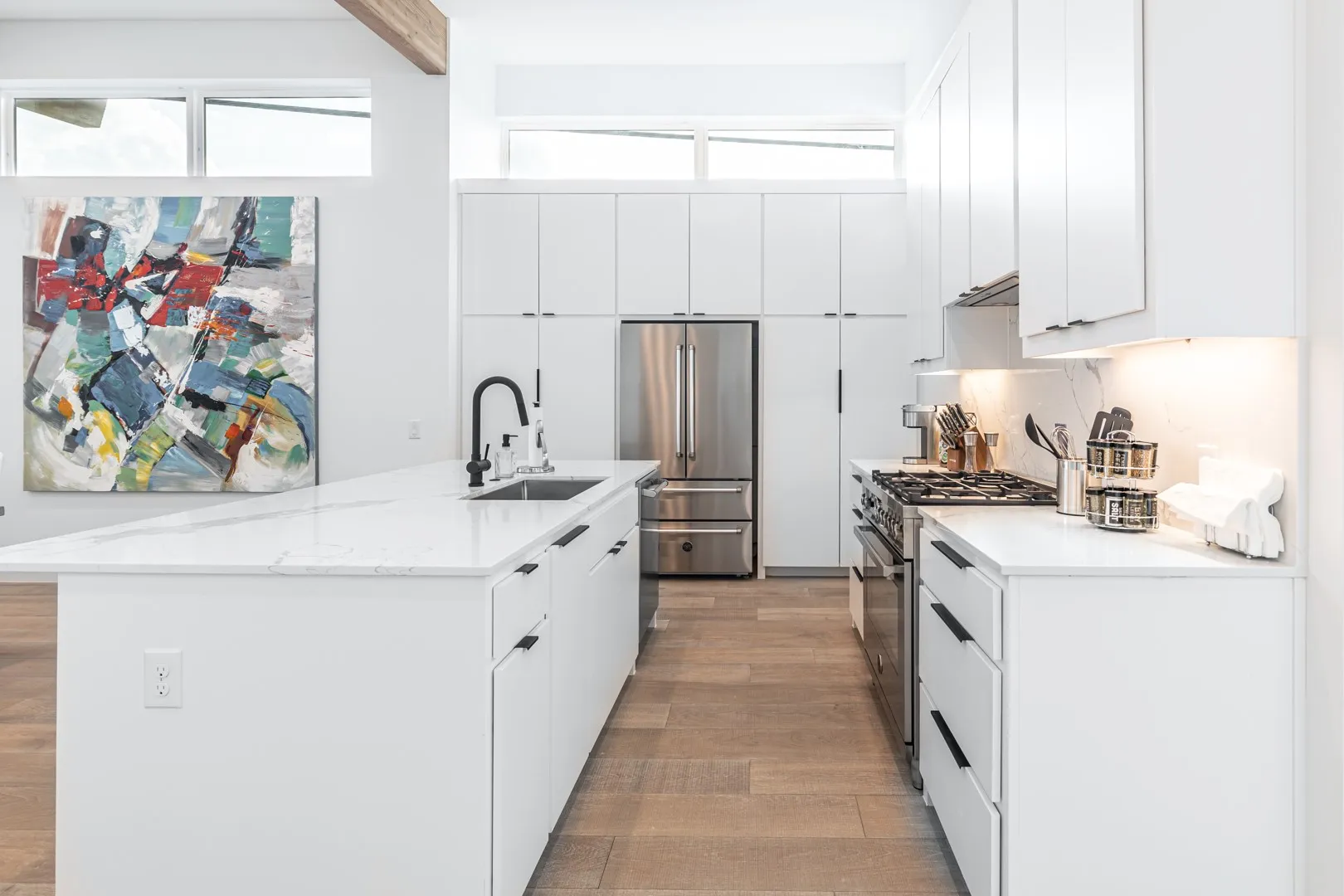 Kitchen featuring premium appliances, light wood-type flooring, white cabinetry, and a center island with sink