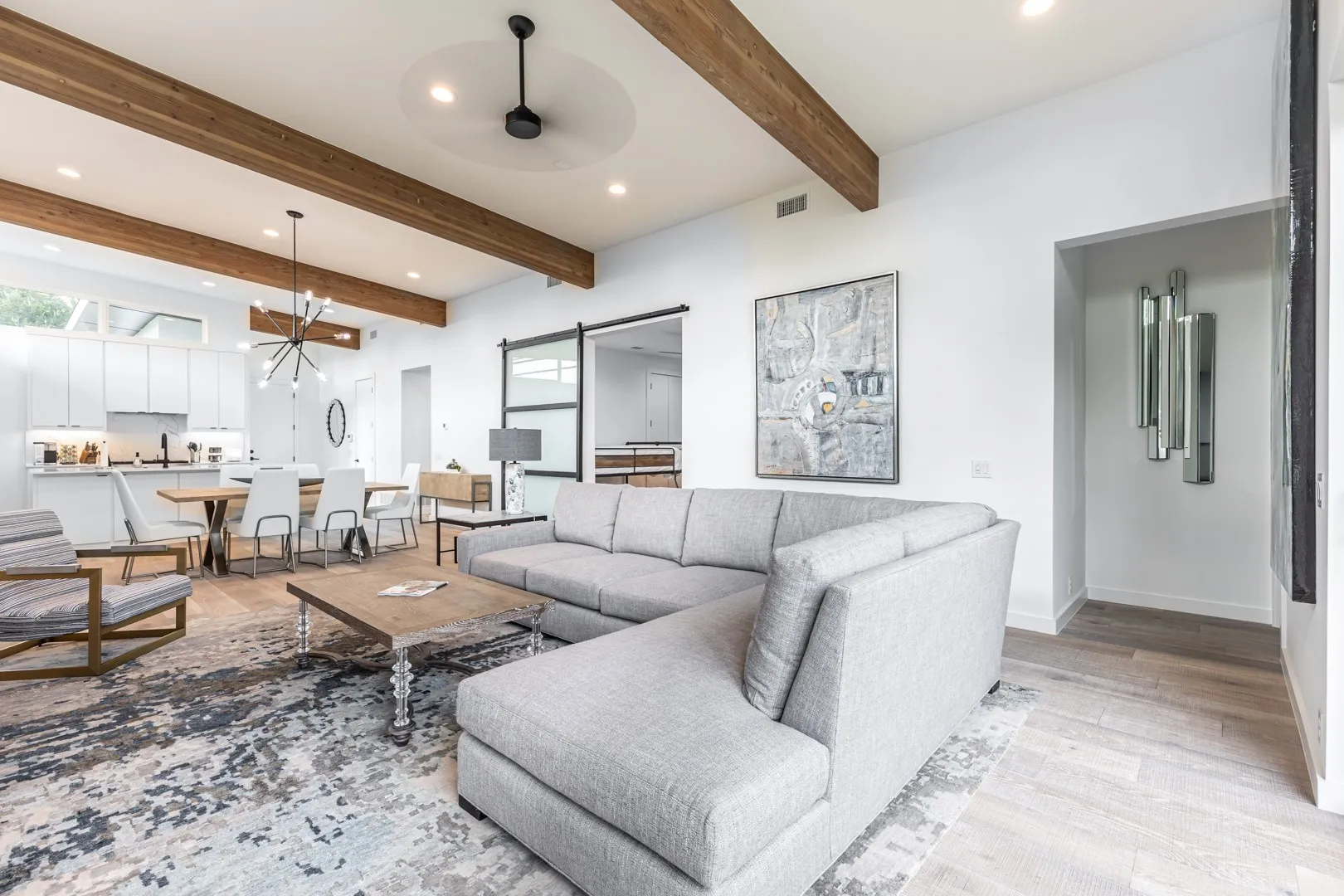 Living room featuring light wood-style flooring, recessed lighting, ceiling fan, beamed ceiling, and a barn door