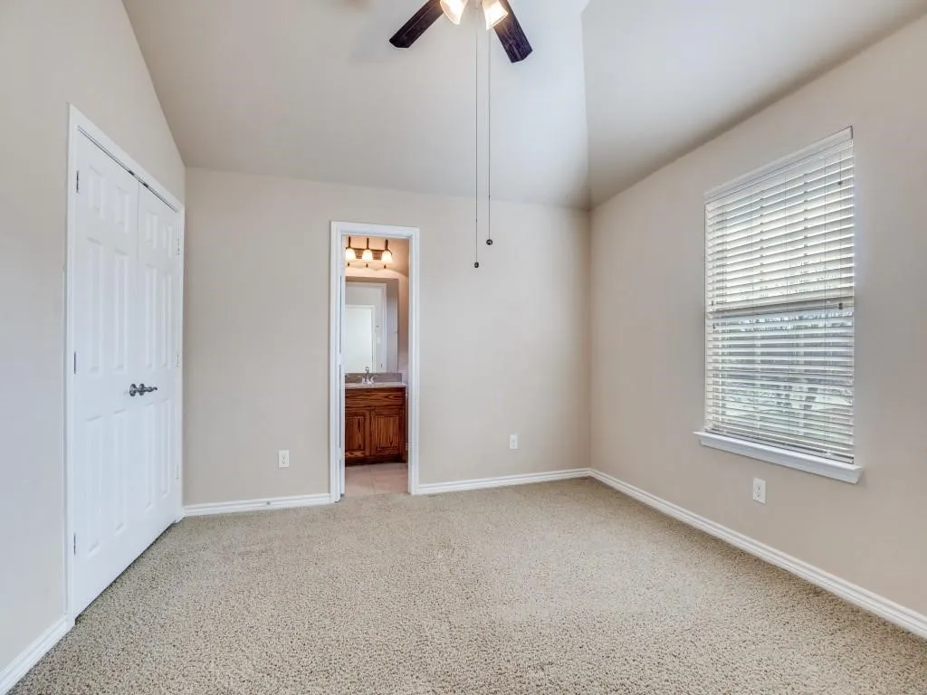 Vaulted ceiling with a ceiling fan, neutral carpet flooring, white trim, and direct access to a bathroom with a wood-finish vanity