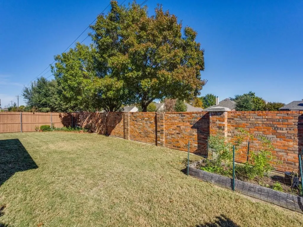 Expansive backyard featuring a manicured lawn, brick perimeter wall, and a raised garden bed