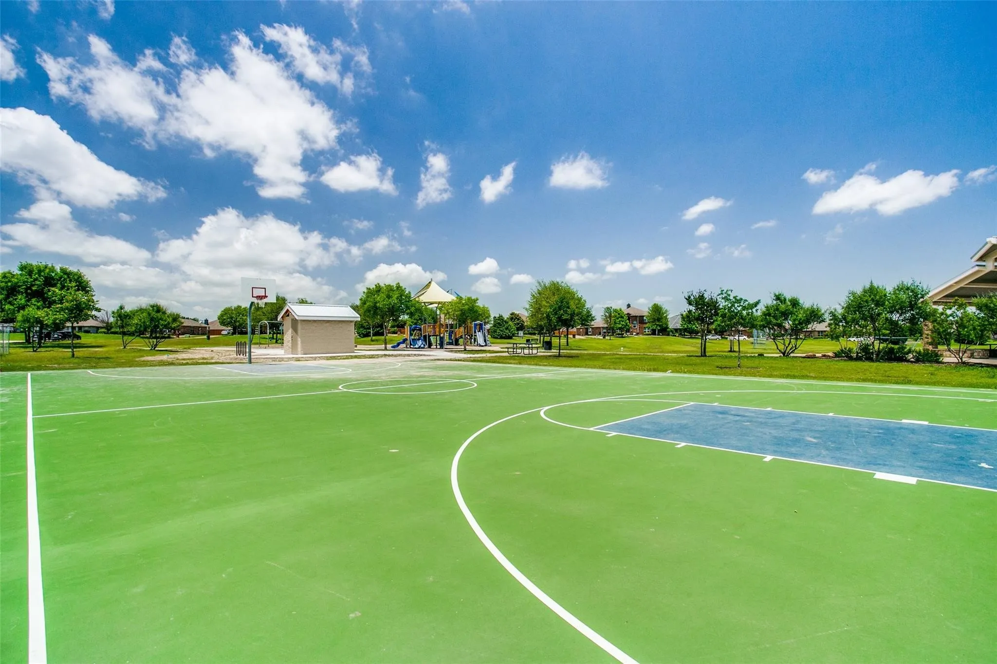 Basketball court with green and blue surfacing, adjacent to a playground and open green space