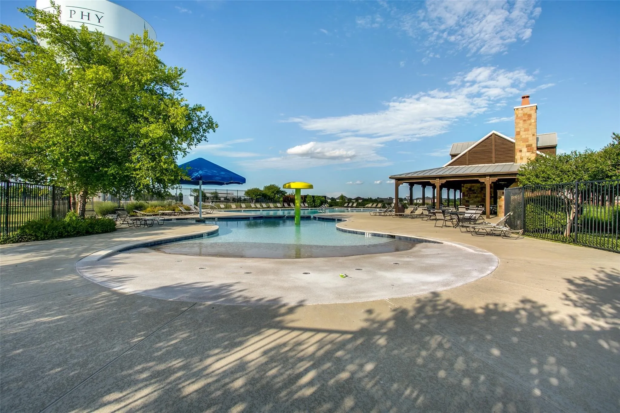 Swimming pool with integrated splash pad, covered patio with wood columns, and stone chimney