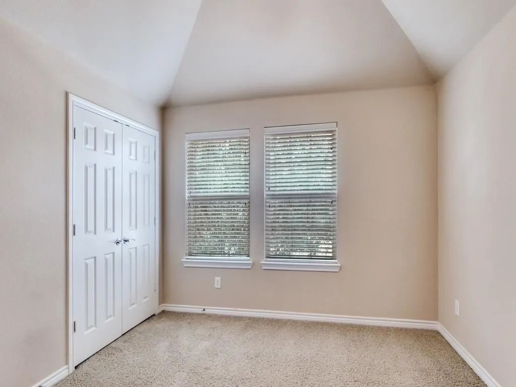 Angled ceiling, dual pane windows with blinds, carpeted flooring, and a paneled bifold door