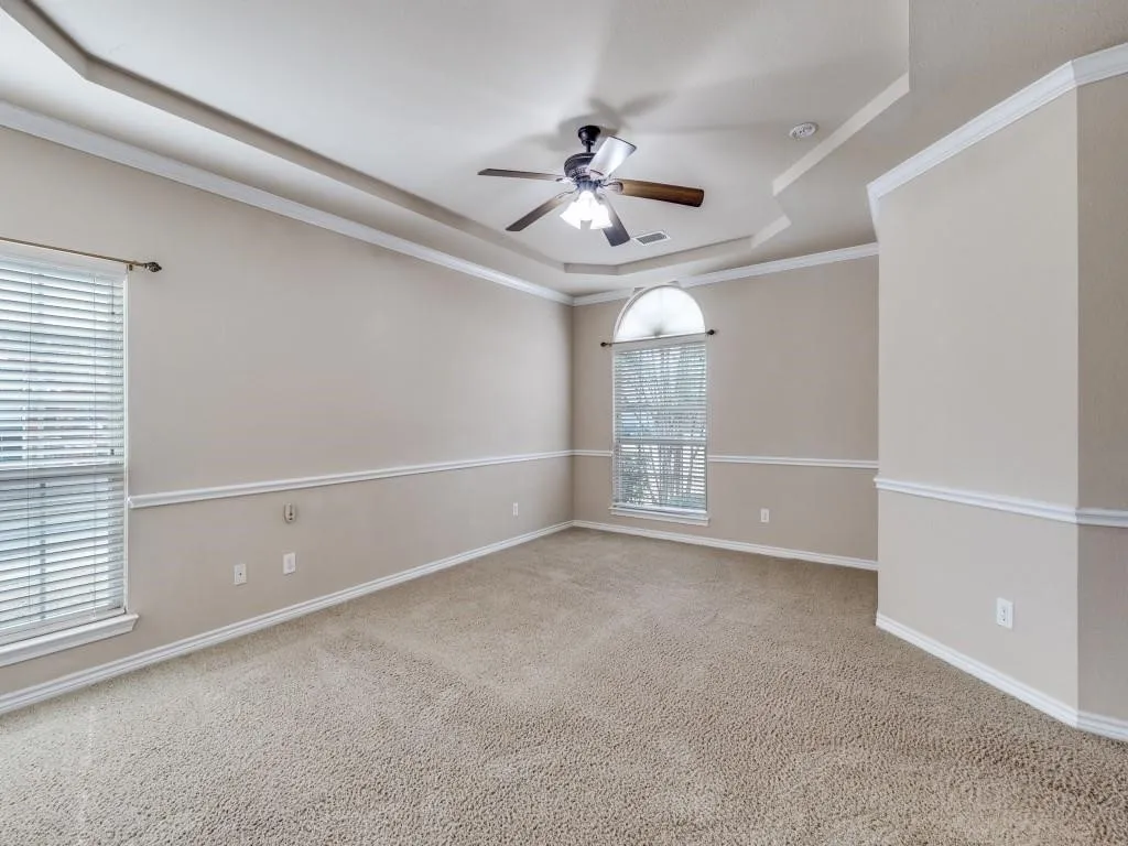 Tray ceiling with crown molding, ceiling fan, arched window, and neutral carpeting