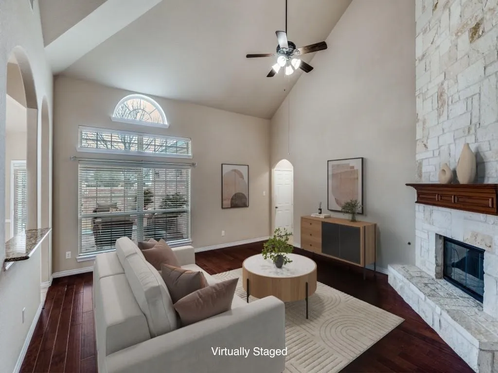 Vaulted ceilings, wood-finish flooring, stone-clad fireplace with wood mantel, large windows with upper arched window, and recessed arched entryway