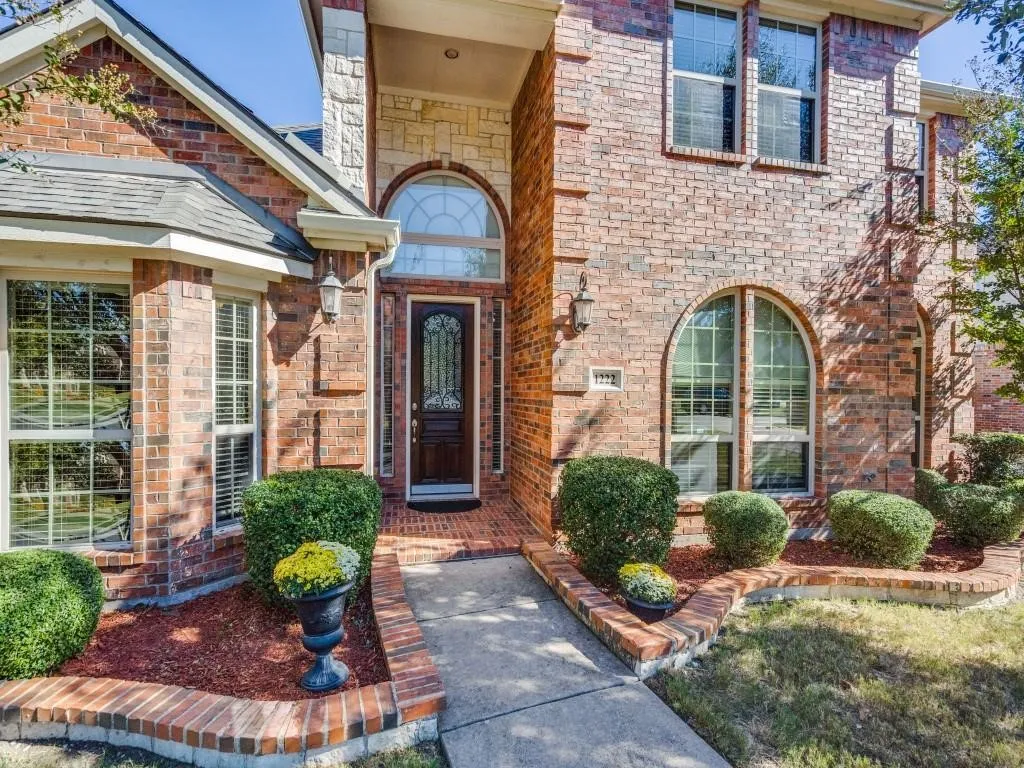 Brick exterior with stone accents, arched windows, an intricate front door, and a concrete pathway leading to the entry