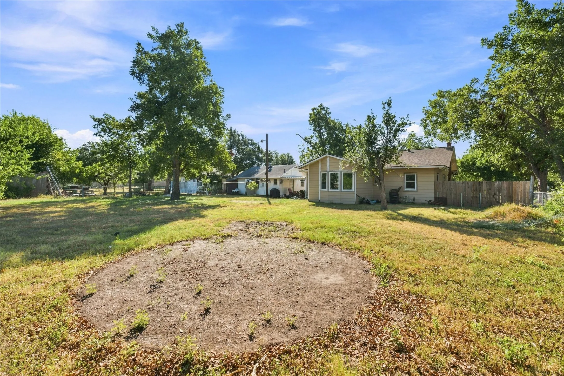 Expansive lot with established trees and a detached structure, featuring a wood fence