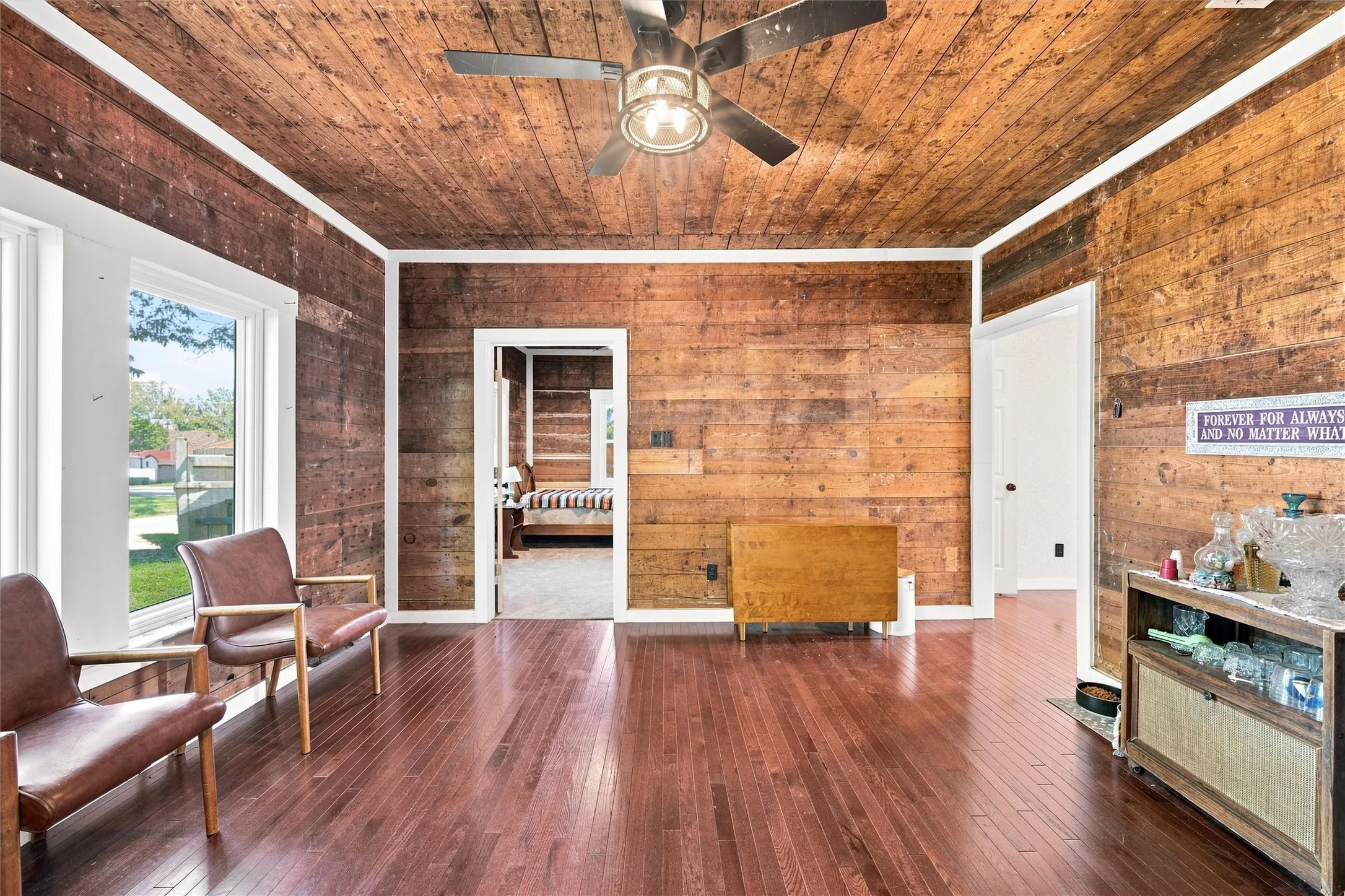 Wood-finish flooring, wood-paneled walls, wood-paneled ceiling, ceiling fan, and white trim accents