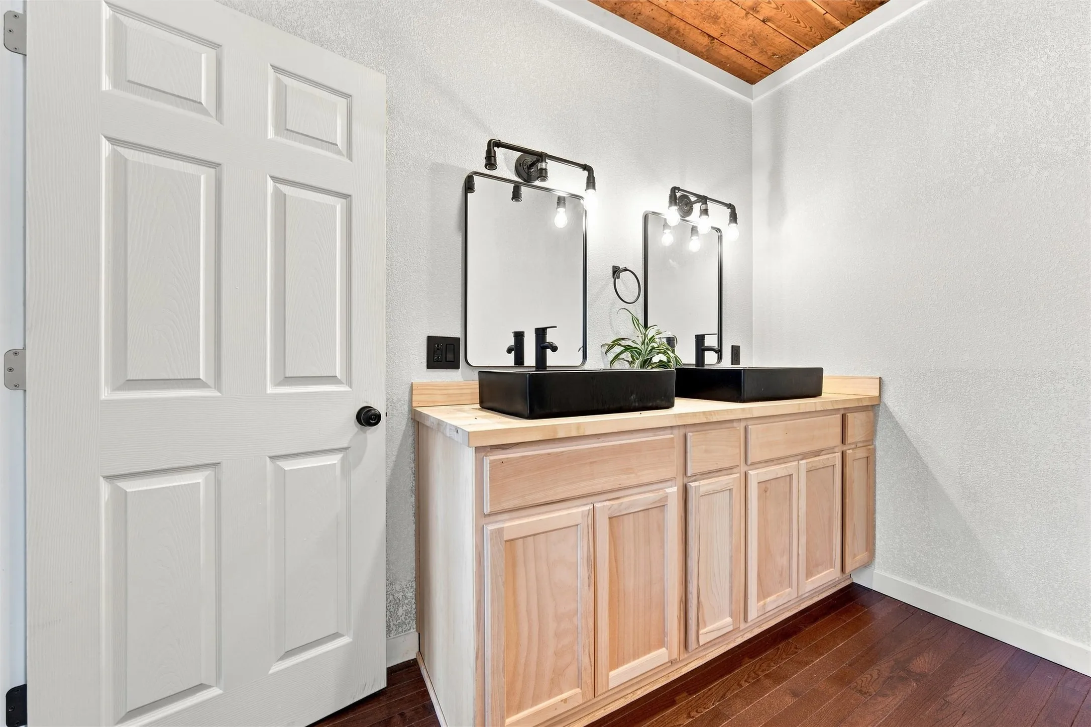 Wood-finish flooring, natural wood vanity, dual rectangular vessel sinks, framed mirrors with industrial-style lighting, and a wood ceiling