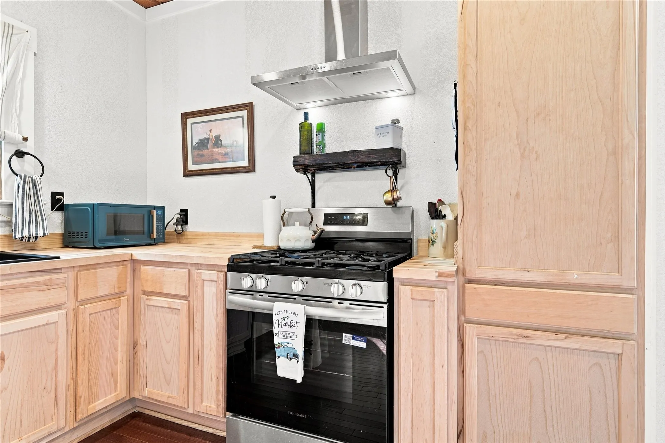 Stainless steel range with a coordinating vent hood, wood-finish cabinetry, and wood-finish countertops