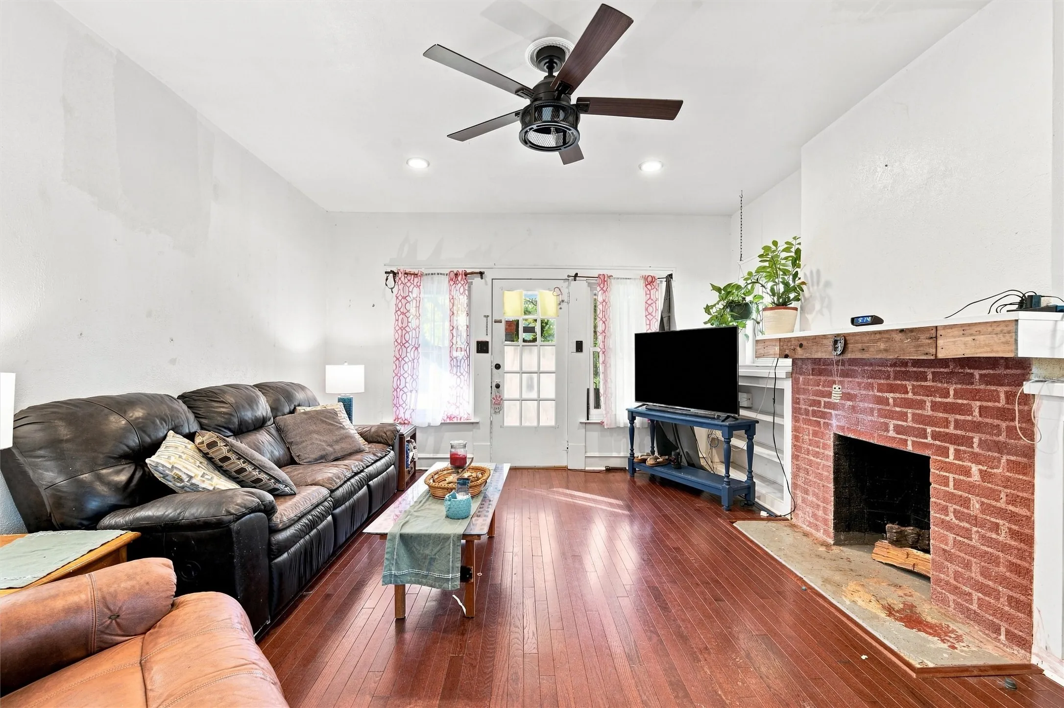 Hardwood flooring, brick fireplace with a wood mantle, ceiling fan, recessed lighting, and a glass-paneled door