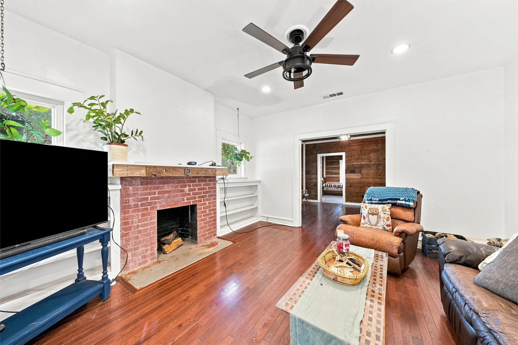 Hardwood flooring, brick-faced fireplace with wood mantel, built-in shelving, recessed lighting, and ceiling fan