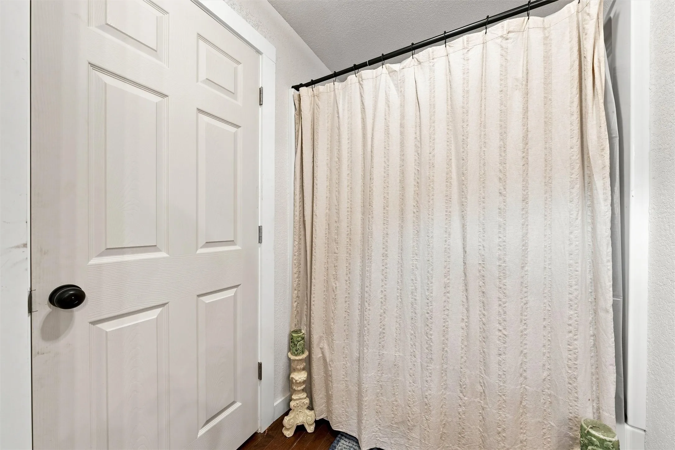 White six-panel door with black hardware, white trim, and a black shower rod