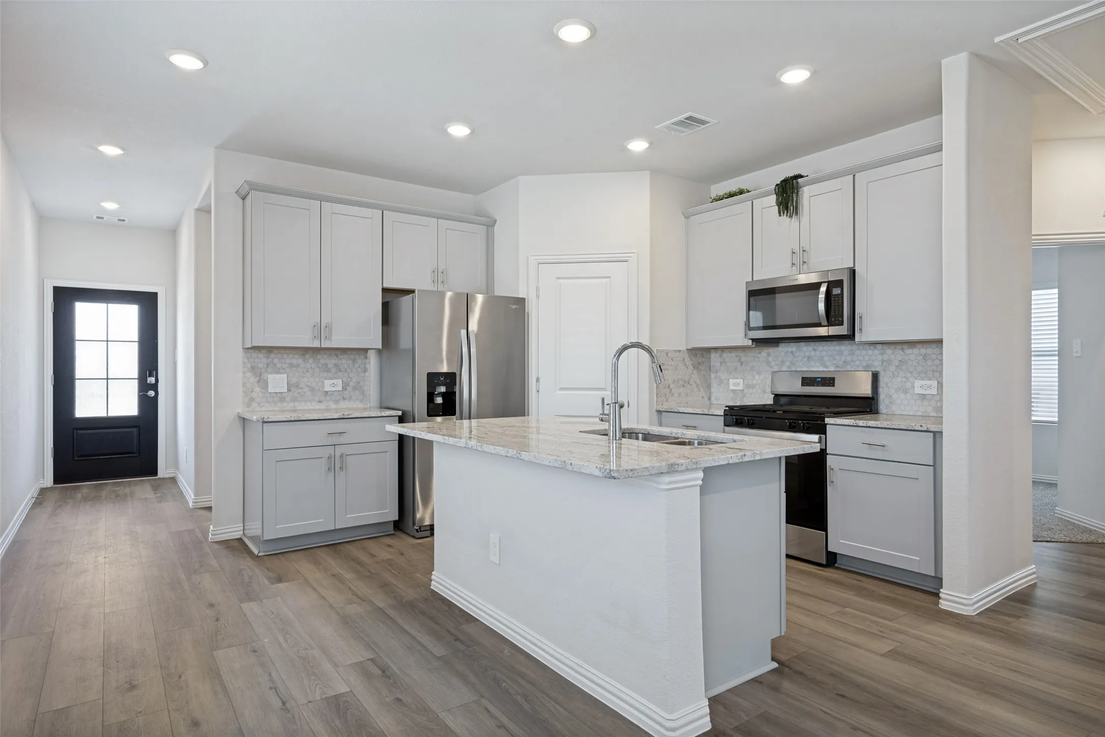 Kitchen island with stainless appliances and fixtures, granite countertops and a tiled backsplash