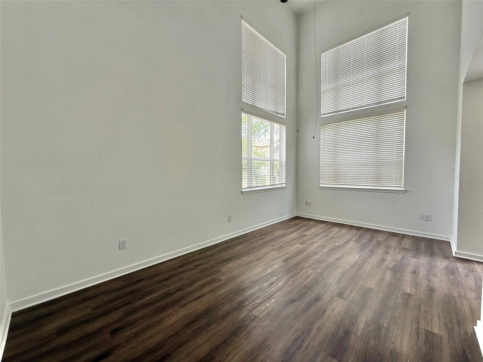 Empty room featuring dark wood-type flooring, baseboards, and a towering ceiling