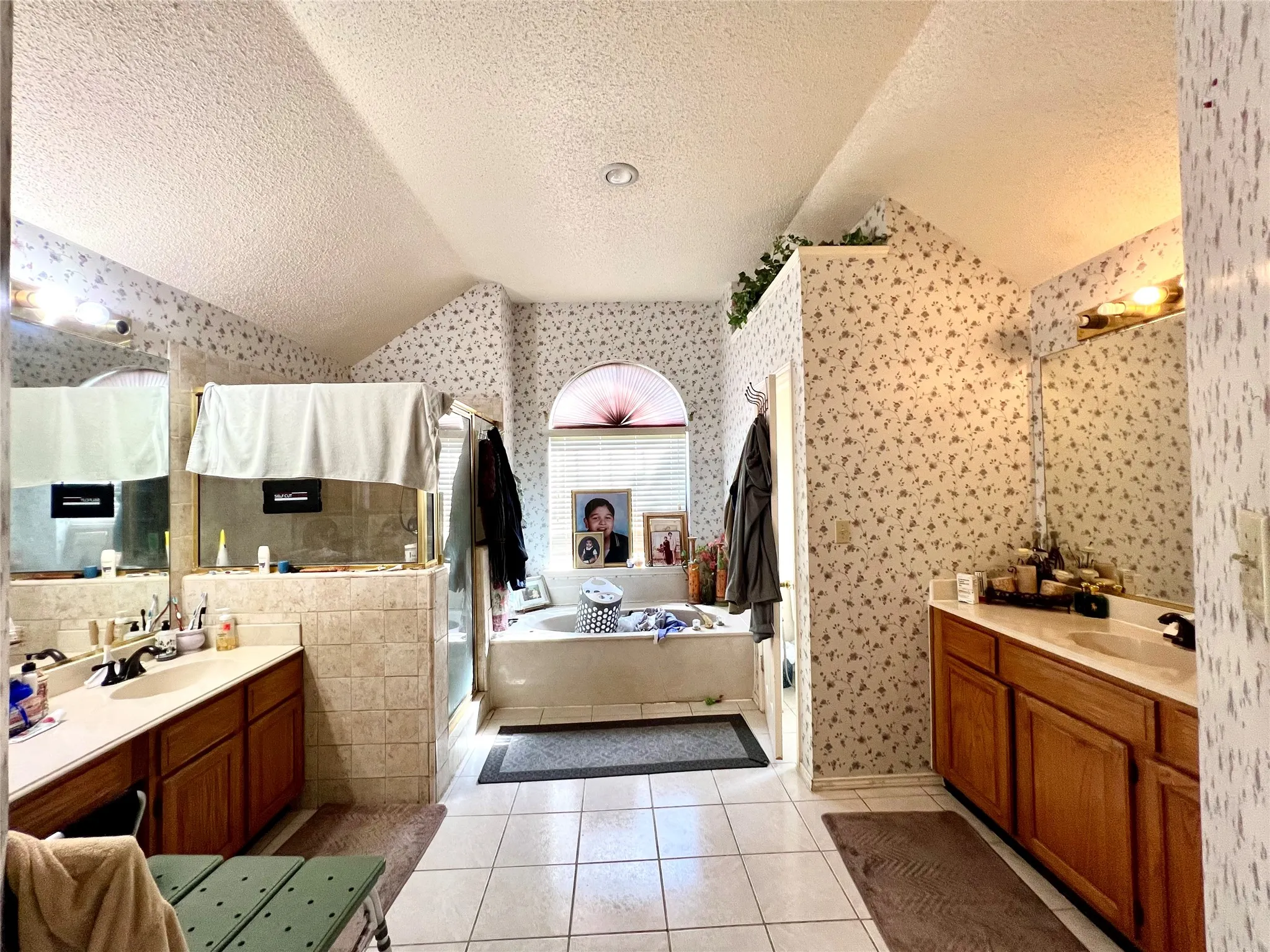 Full bathroom featuring wallpapered walls, lofted ceiling, a textured ceiling, tile patterned floors, and a bath