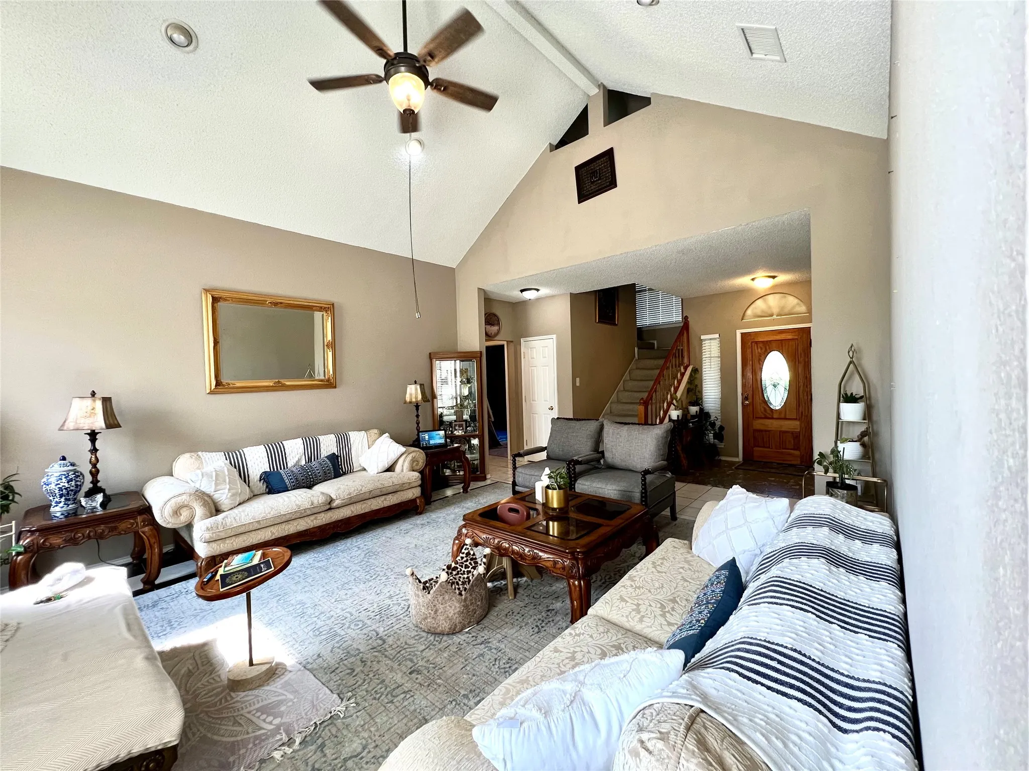 Living area with a ceiling fan, high vaulted ceiling, beam ceiling, stairs, and carpet floors