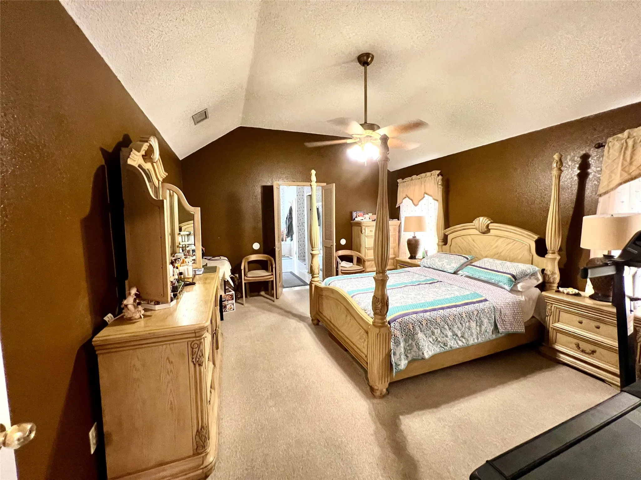 Bedroom with a textured ceiling, light colored carpet, vaulted ceiling, and a ceiling fan