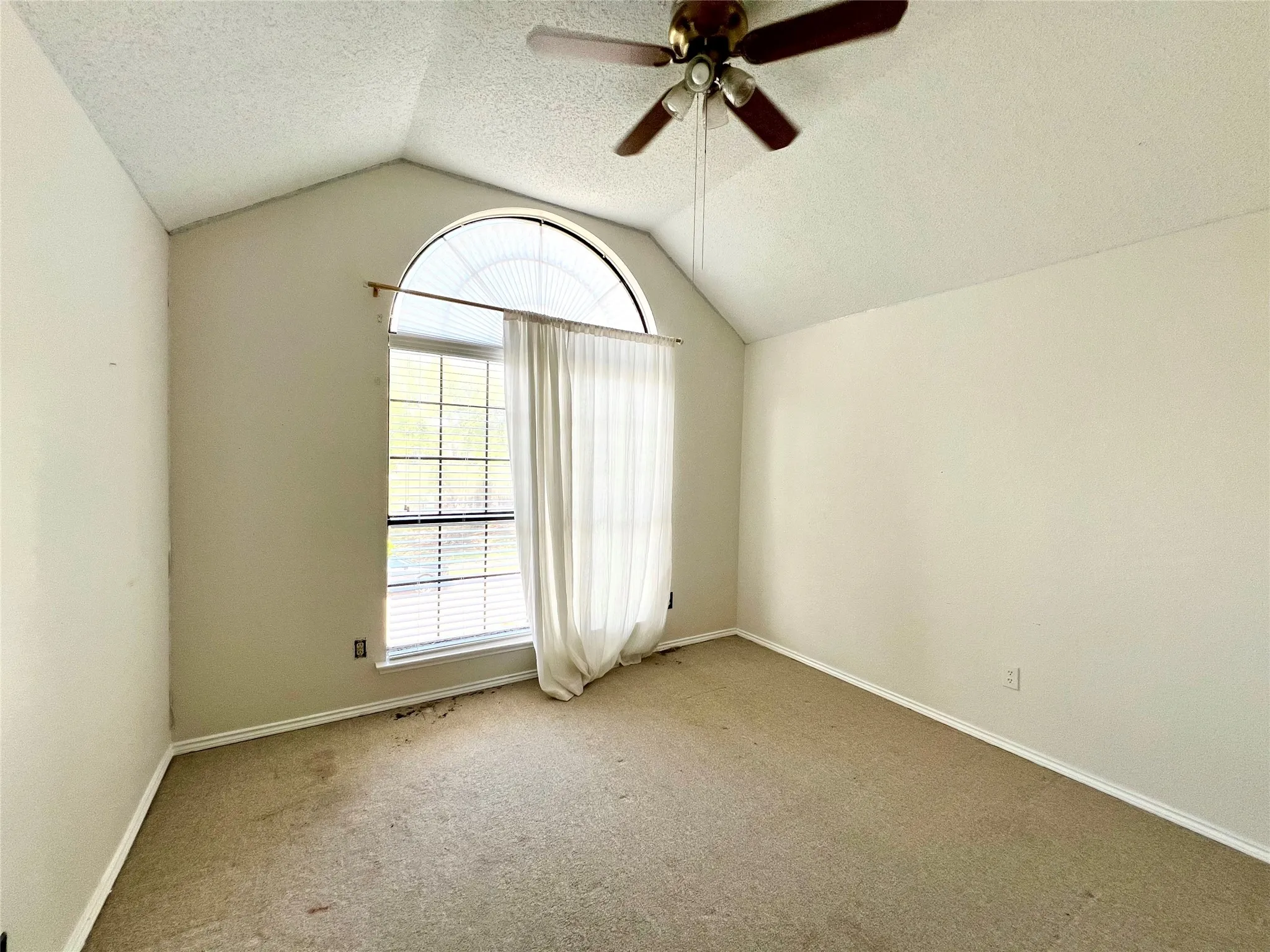 Carpeted spare room featuring a ceiling fan, vaulted ceiling, a textured ceiling, and healthy amount of natural light