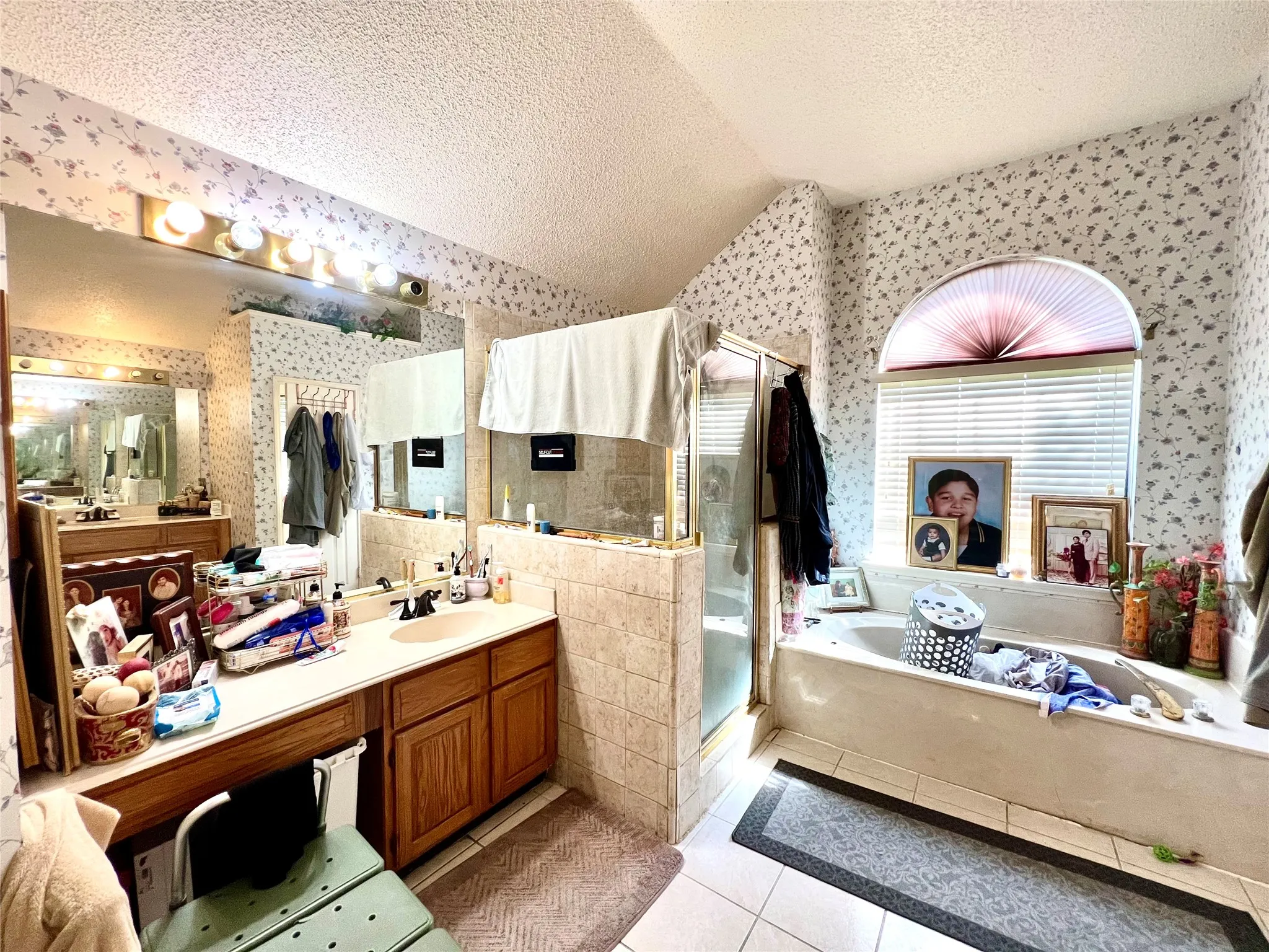 Bathroom with wallpapered walls, a textured ceiling, a bath, a shower stall, and tile patterned flooring