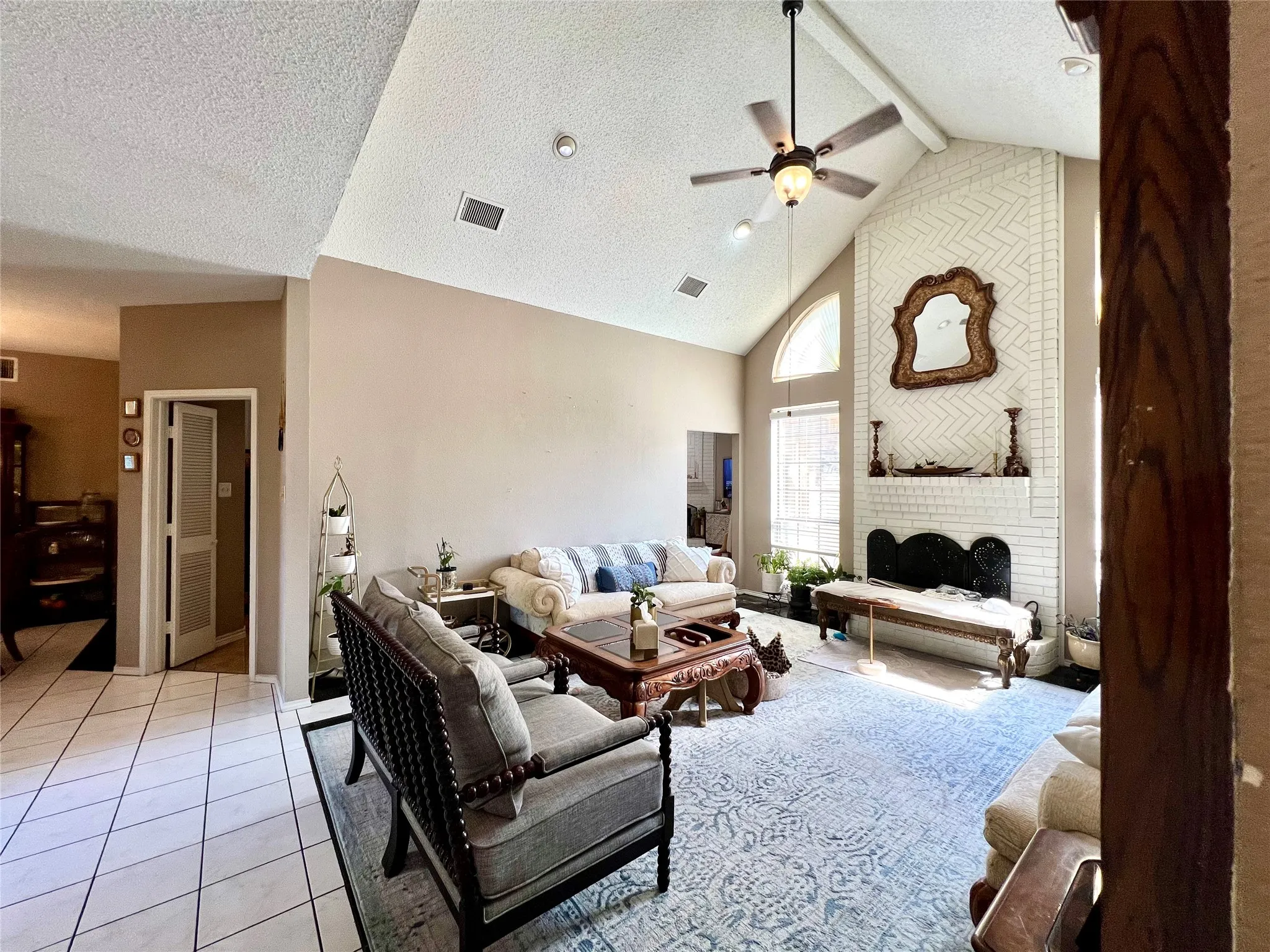 Living area featuring a ceiling fan, high vaulted ceiling, a textured ceiling, light tile patterned floors, and beam ceiling