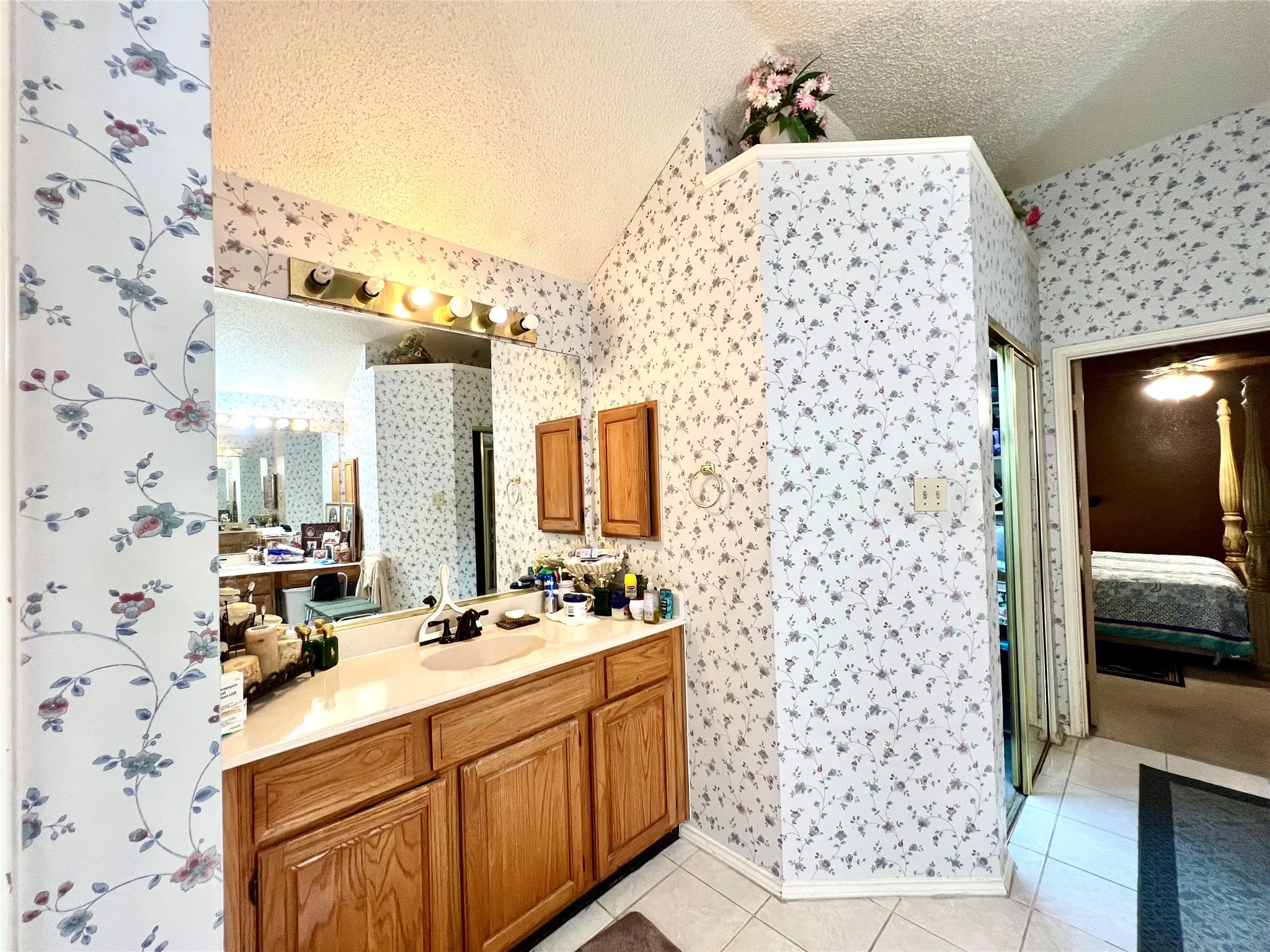 Ensuite bathroom featuring wallpapered walls, a textured ceiling, vanity, vaulted ceiling, and tile patterned flooring