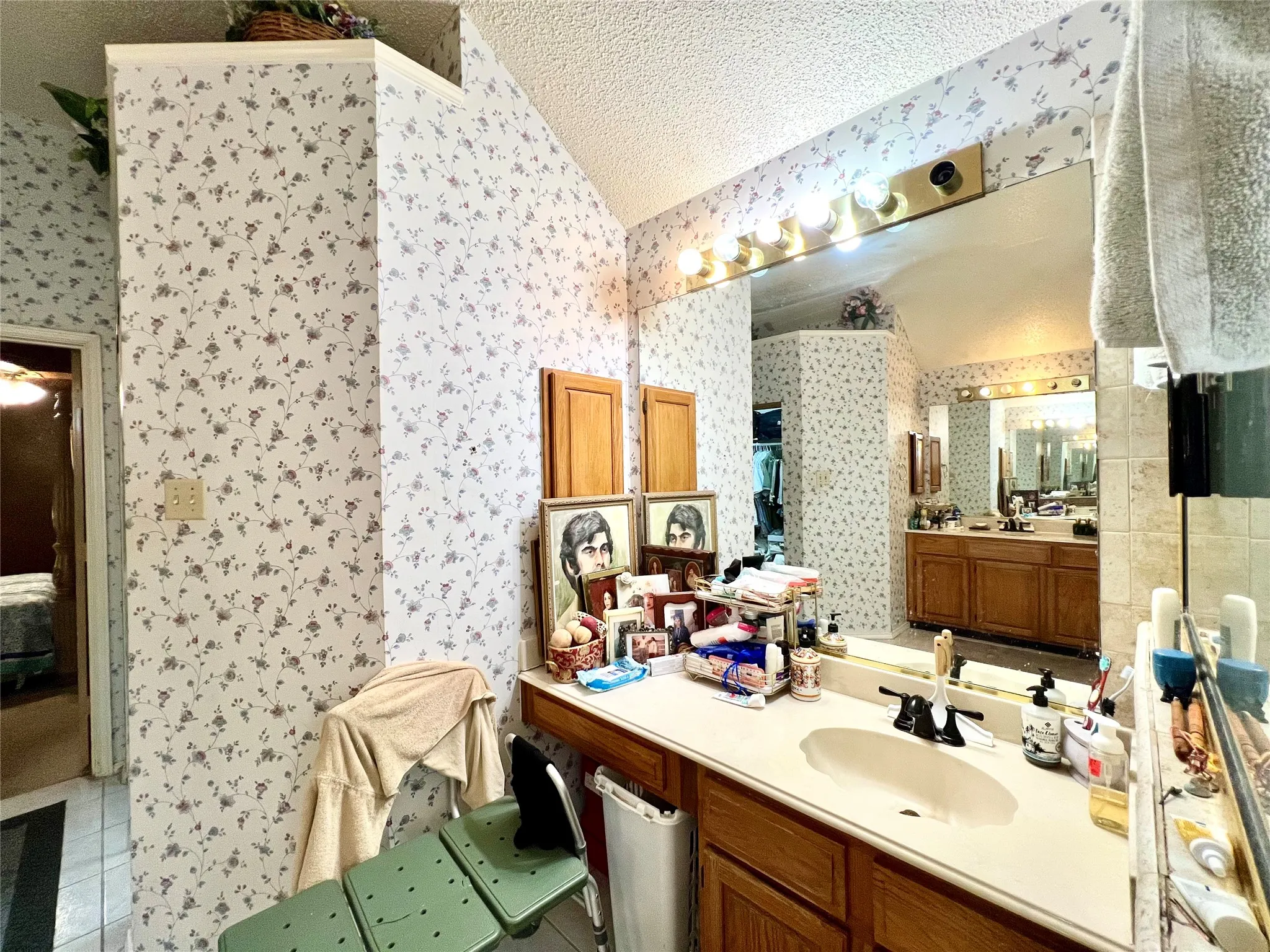 Full bathroom with wallpapered walls, lofted ceiling, tile patterned flooring, vanity, and a textured ceiling