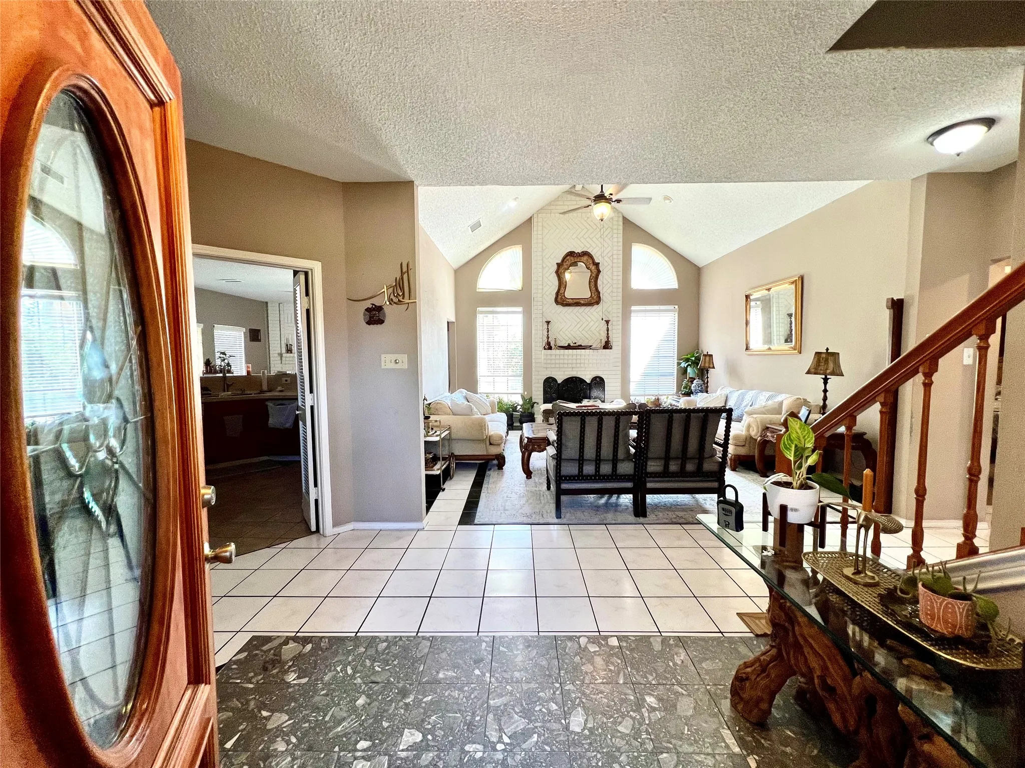 Foyer entrance featuring a ceiling fan, lofted ceiling, light tile patterned floors, and a textured ceiling