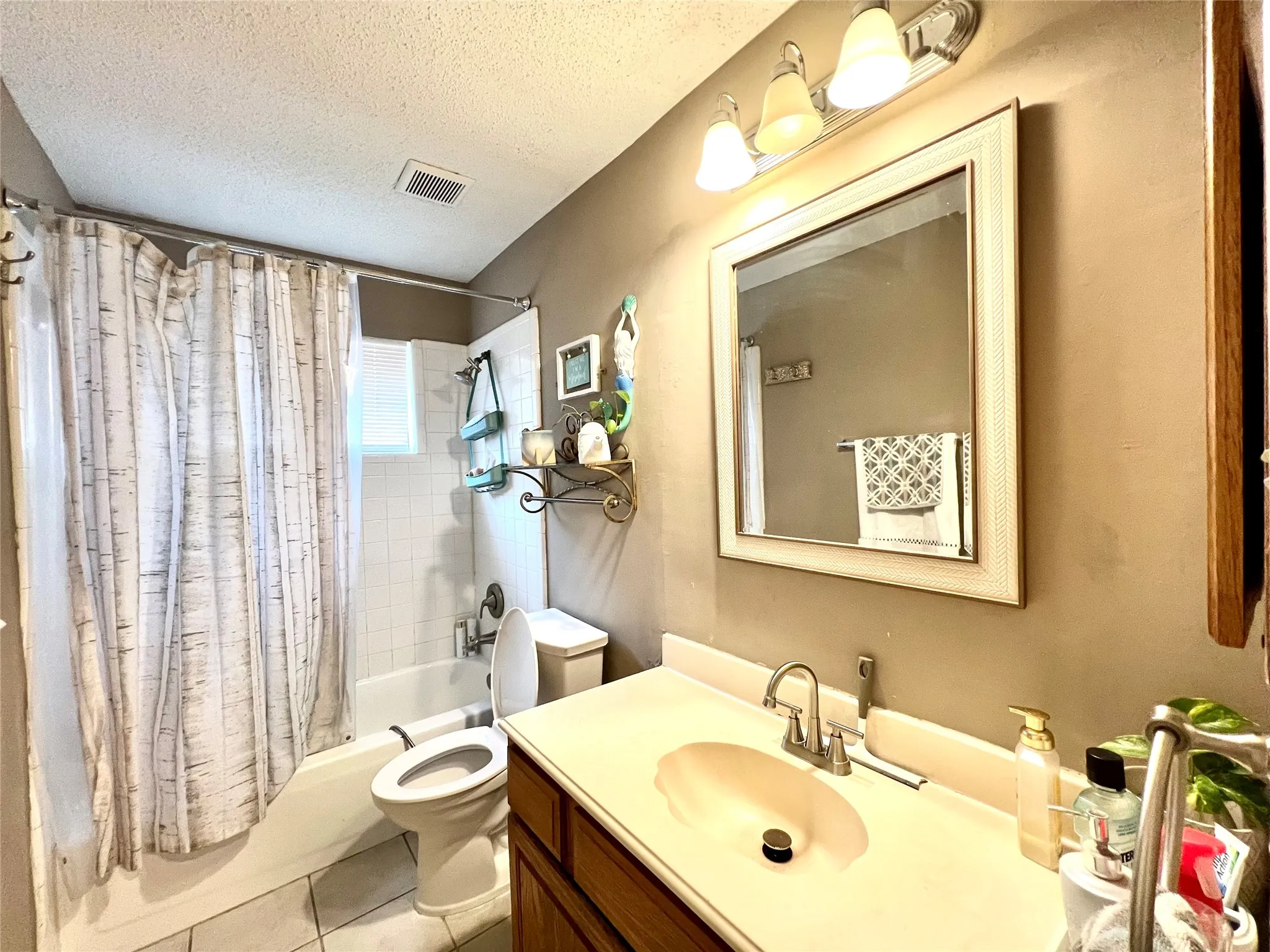 Full bath with shower / tub combo with curtain, vanity, a textured ceiling, and tile patterned flooring