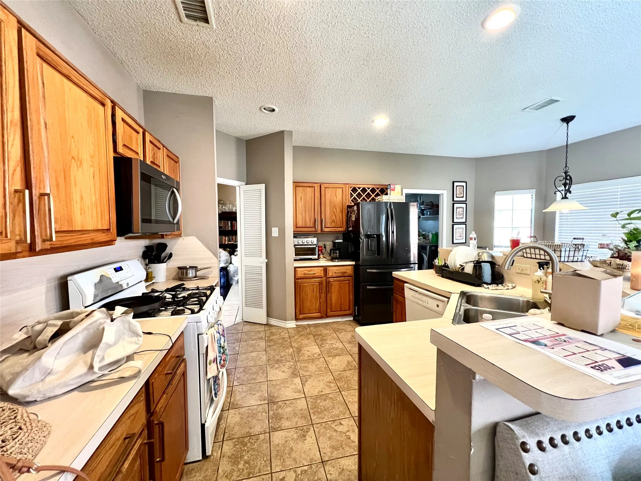 Kitchen featuring white appliances, light countertops, brown cabinetry, a textured ceiling, and hanging light fixtures