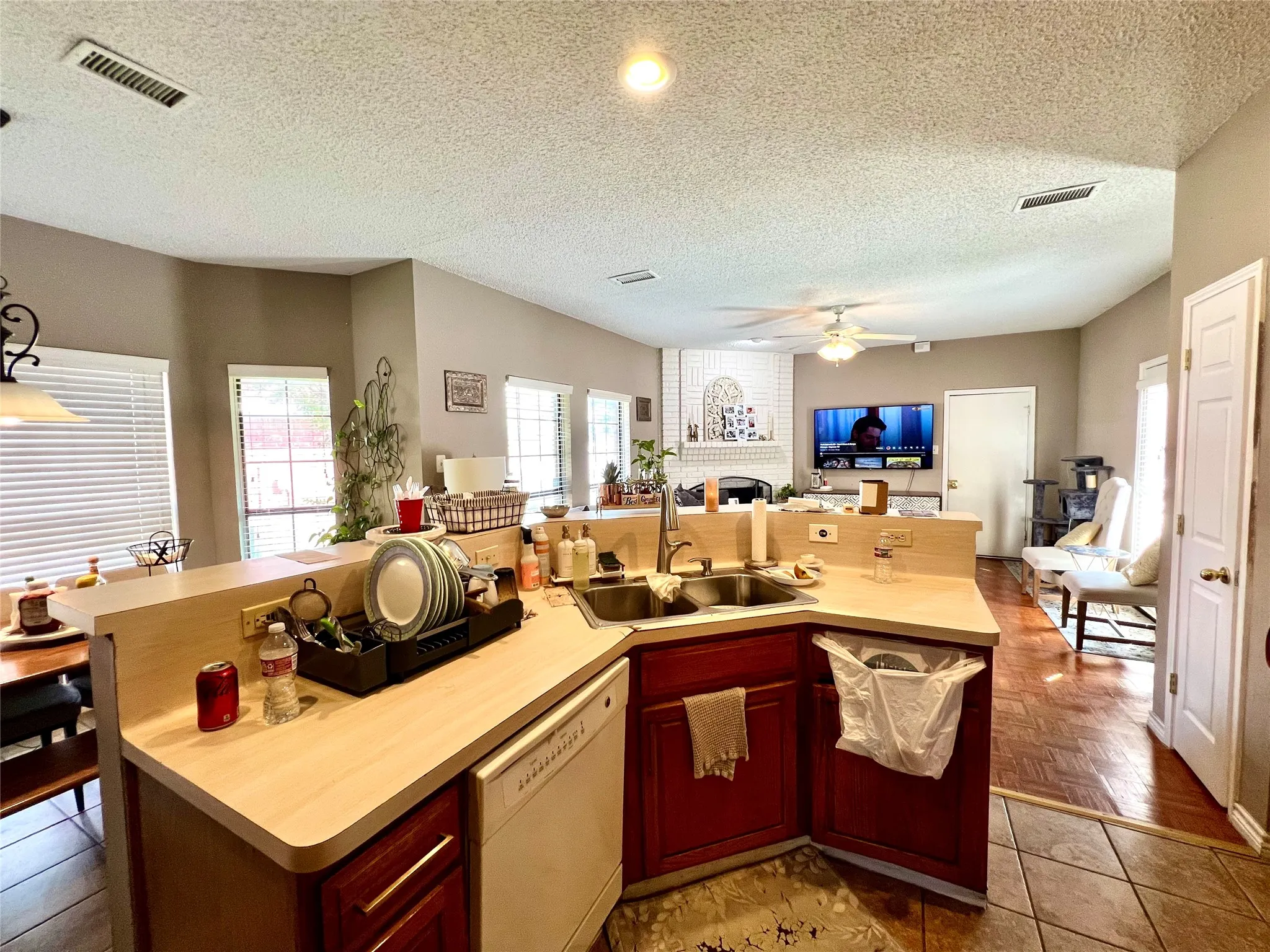 Kitchen with white dishwasher, open floor plan, ceiling fan, a fireplace, and reddish brown cabinets