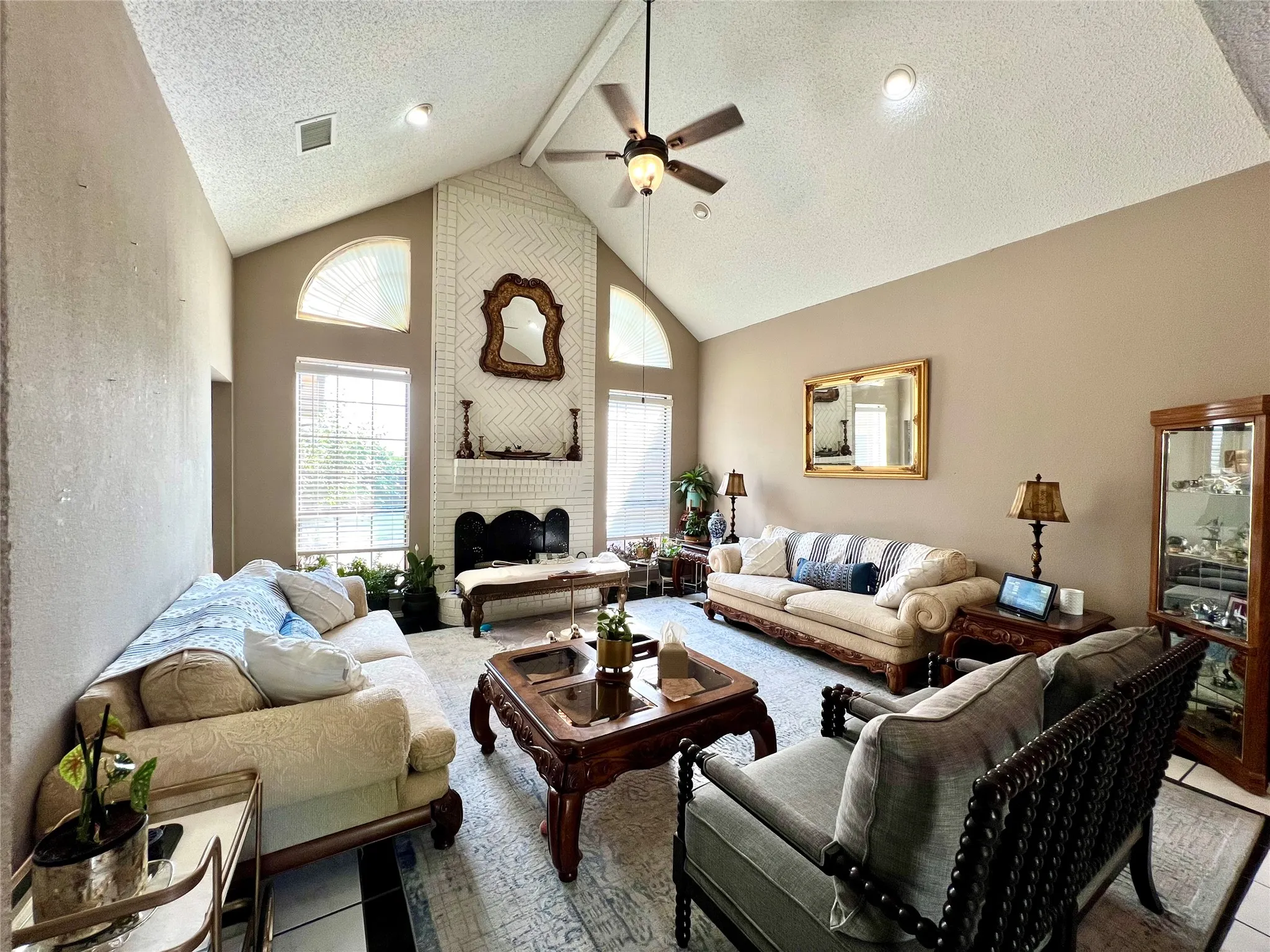 Living area featuring ceiling fan, high vaulted ceiling, a textured ceiling, and a fireplace