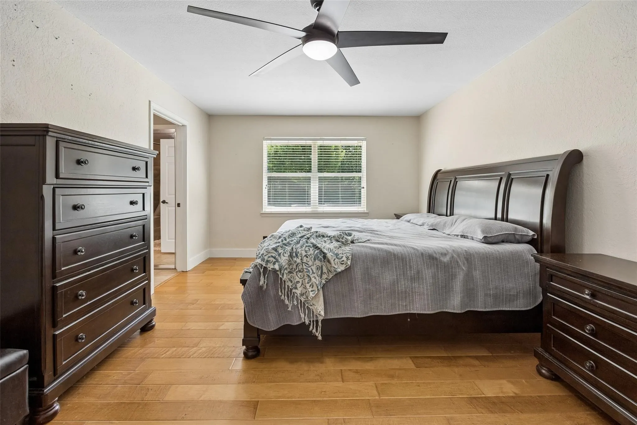Bedroom featuring wood-finish flooring, a window with blinds, a ceiling fan with integrated lighting, and neutral wall tones