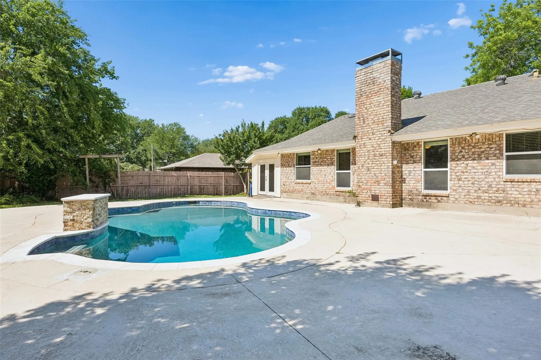 Resort-style backyard oasis featuring a custom free-form swimming pool with sun shelf, surrounding concrete decking, and mature landscaping