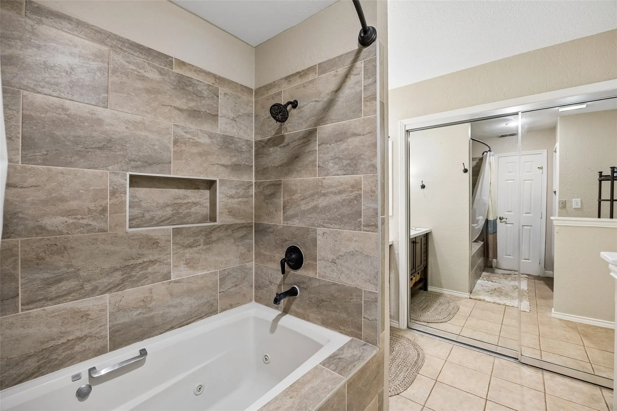 Tiled shower and jetted tub featuring a recessed niche and matte black fixtures