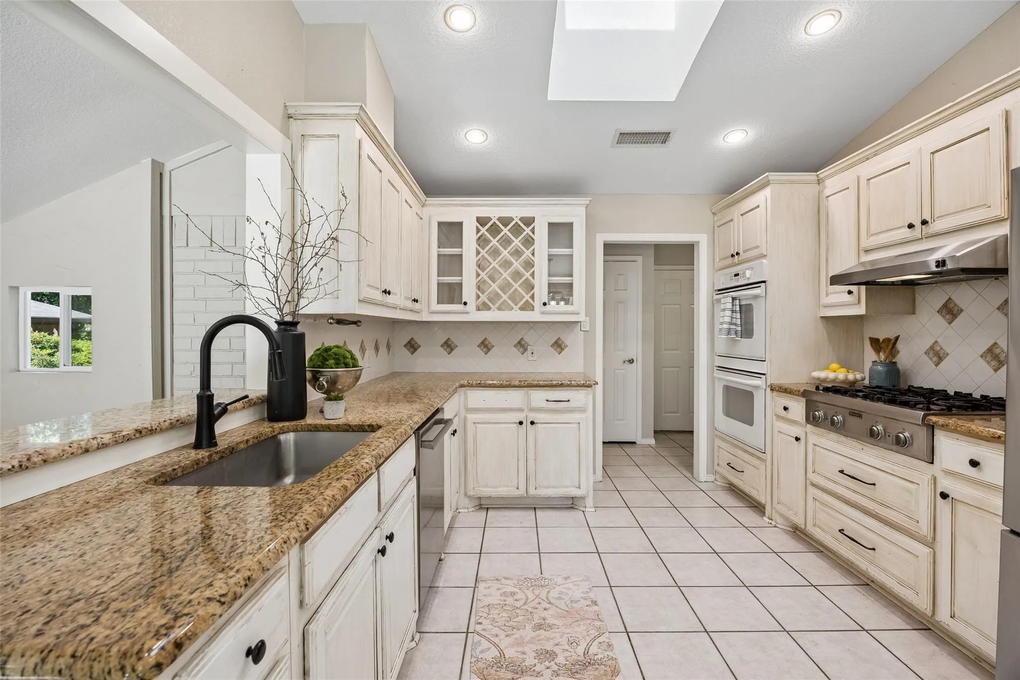 Kitchen featuring granite countertops, a gas range with a stainless steel vent hood, double wall ovens, a skylight, and recessed lighting