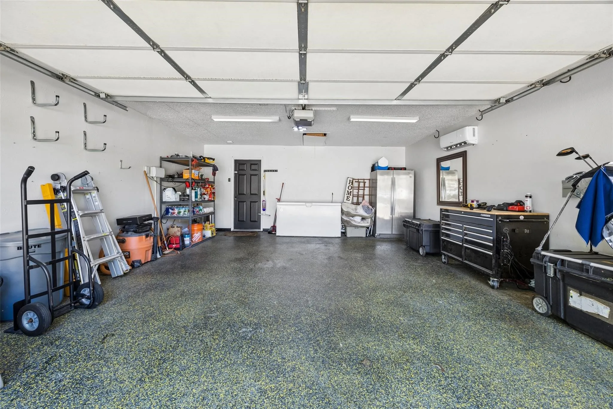 Spacious garage featuring epoxy-coated flooring, recessed LED lighting, wall-mounted storage hooks, and built-in cabinetry