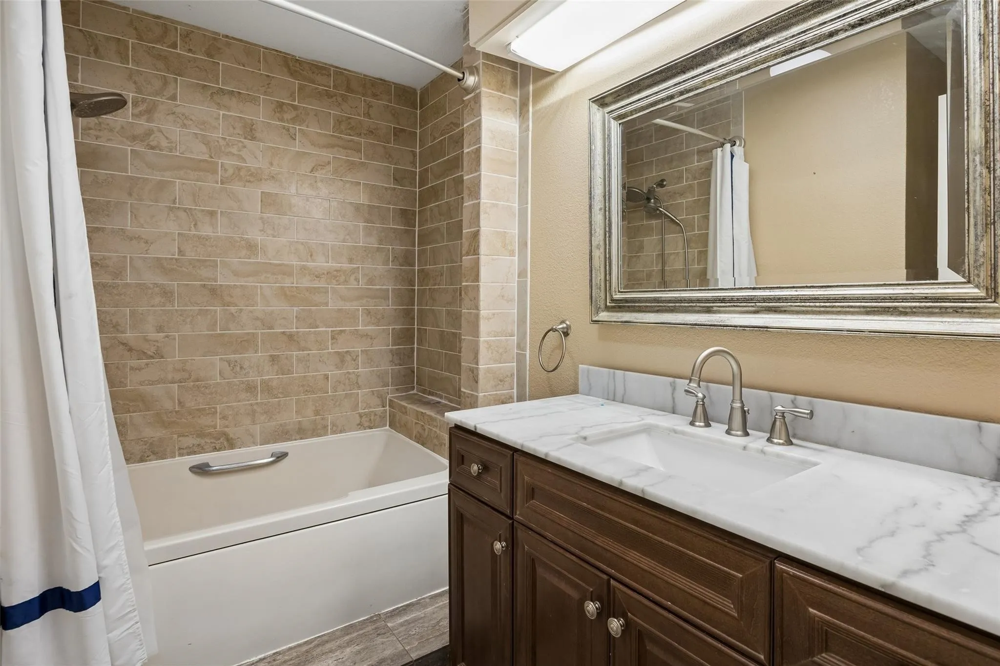 Bathroom featuring a vanity with a white countertop and undermount sink, a large framed mirror, and a tiled shower-tub combination with a grab bar