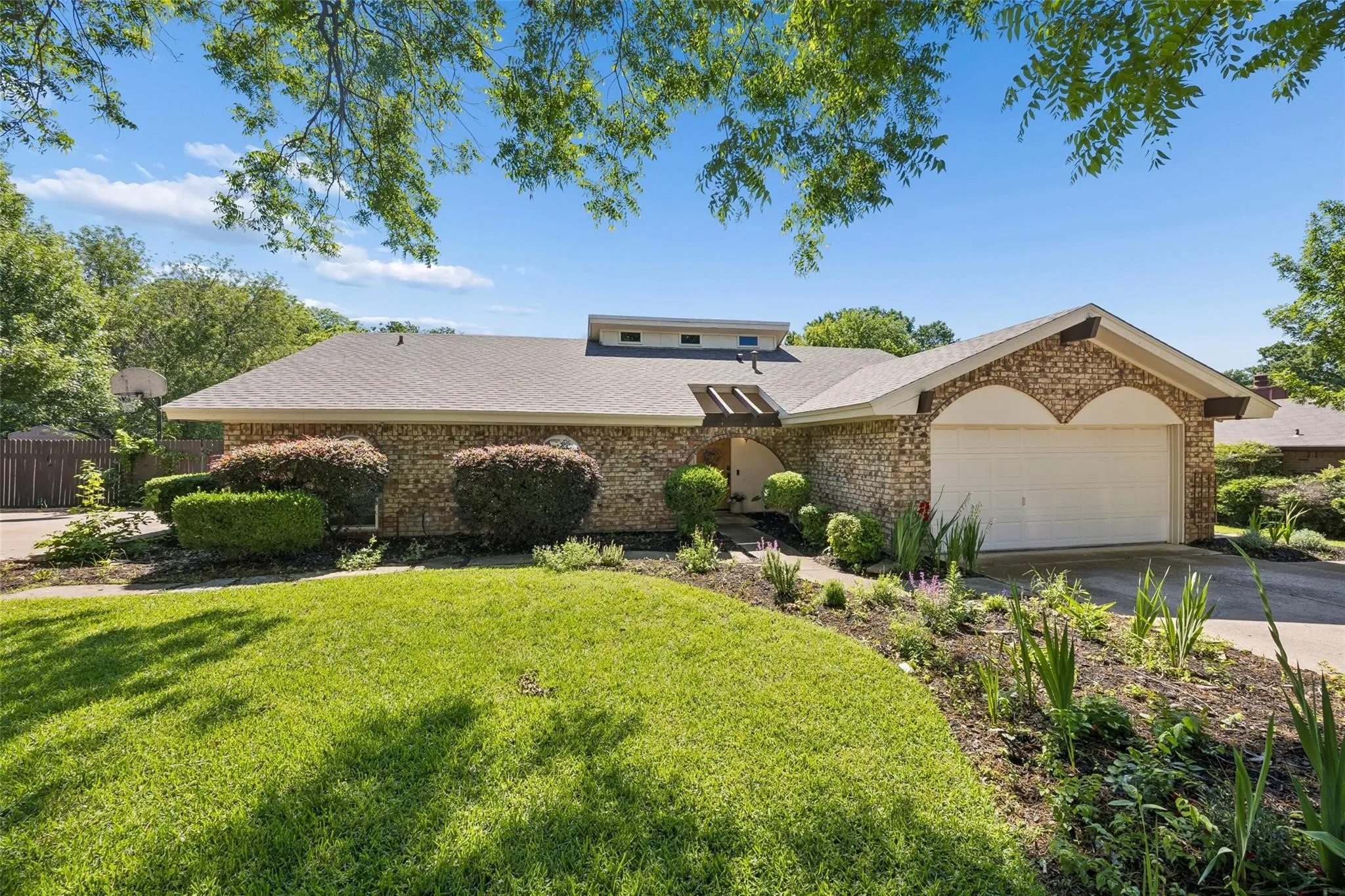 Brick facade home featuring a two-car garage with arched accents, a paved driveway, and a front lawn with established landscaping