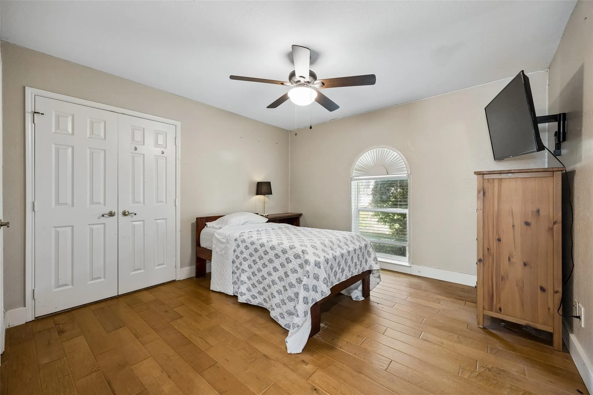 Room featuring wood-finish flooring, a ceiling fan with integrated lighting, and a white arched window with blinds