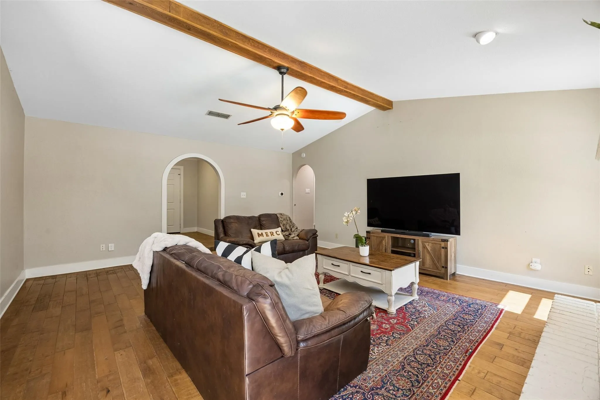 Vaulted ceiling with exposed wood beams, wood-finish flooring, and white baseboards