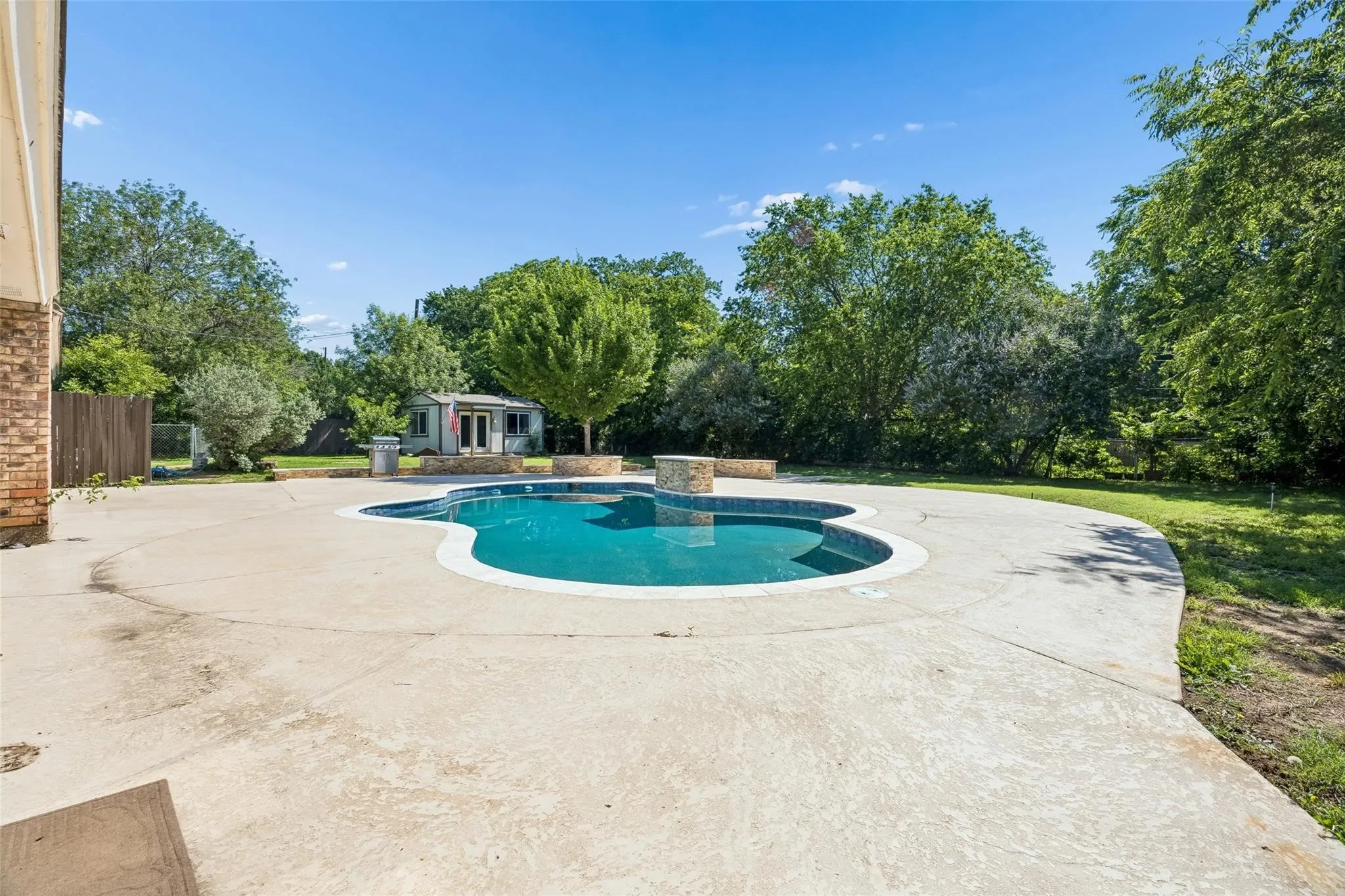 Kidney-shaped swimming pool with stone coping and surrounding concrete patio