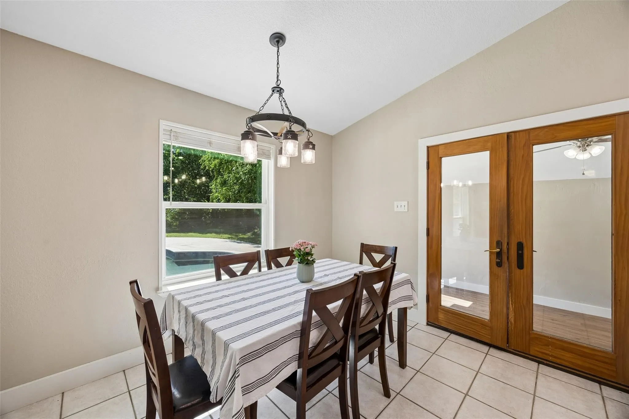 Dining area featuring neutral wall paint, tile flooring, a window overlooking a pool, and double glass-paneled doors