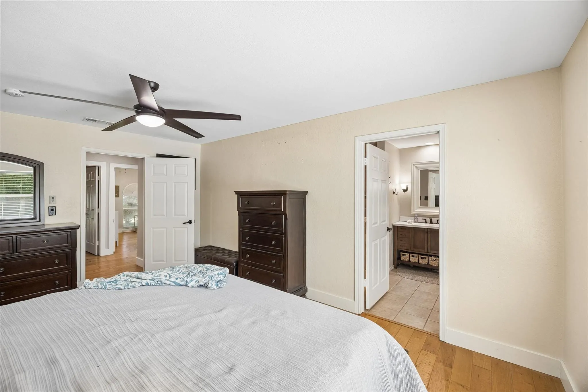 Bright bedroom space featuring light-toned wall paint, wood-finish flooring, and a contemporary ceiling fan