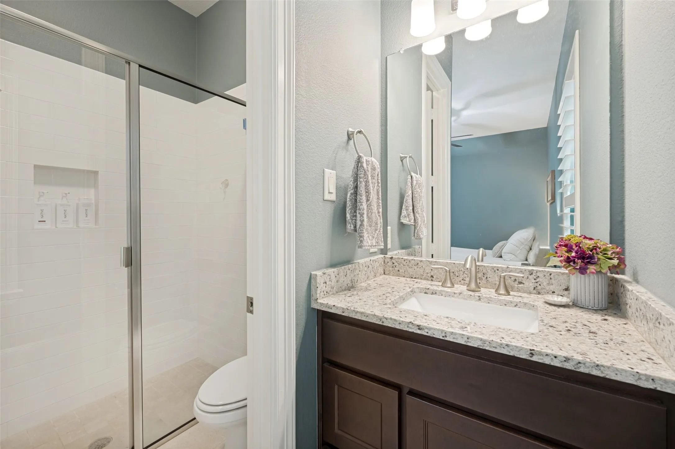 A beautifully appointed guest ensuite bath offers privacy and convenience with a granite-topped vanity, spacious walk-in shower with glass enclosure, and built-in shower niche. Clean finishes and a thoughtful layout create a bright, polished space perfect for overnight guests.