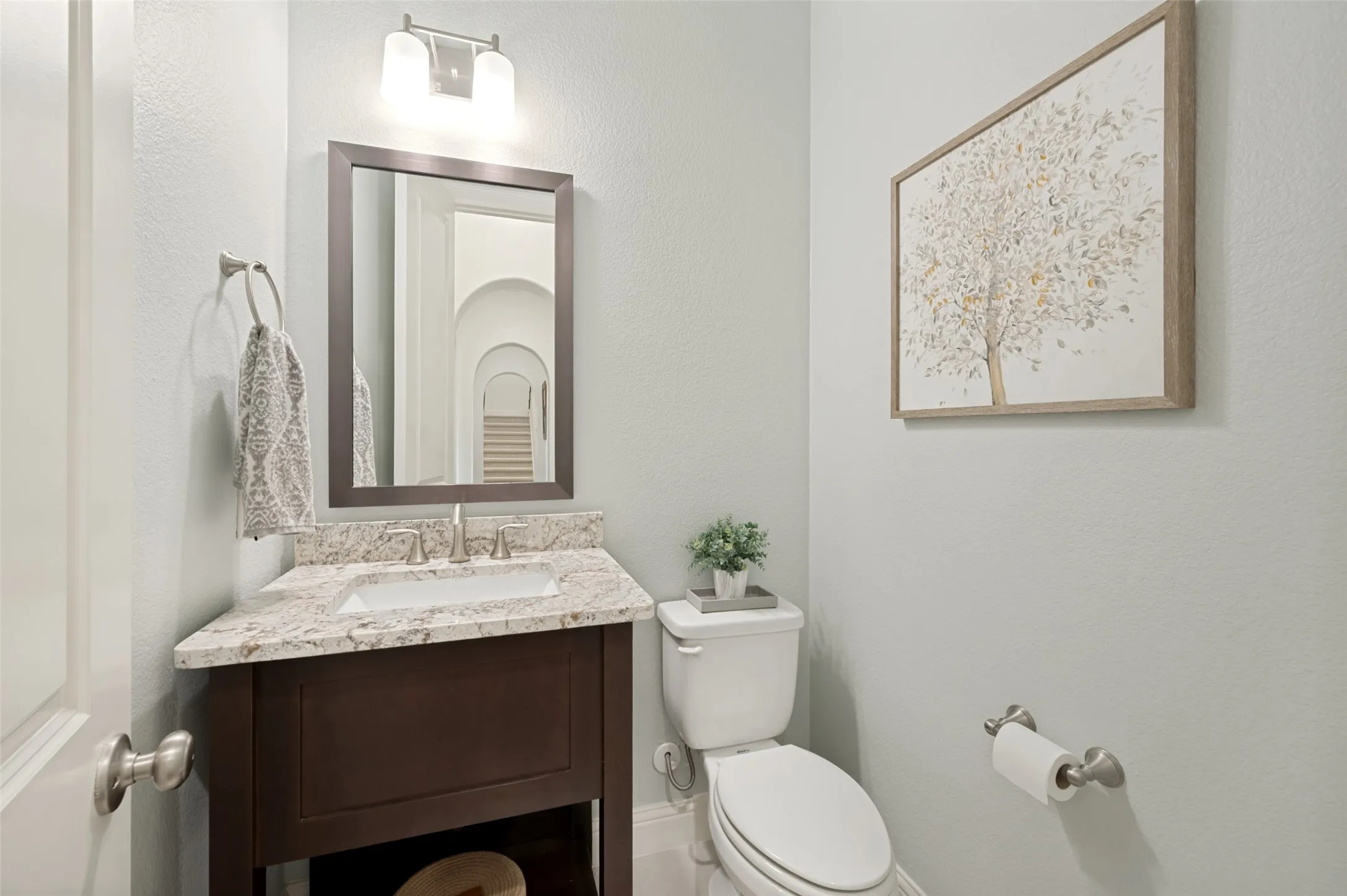 This charming half bath offers a polished space for guests with a granite countertop, rich wood vanity, framed mirror, and elegant fixtures. Soft neutral tones and tasteful finishes create a warm, inviting feel.