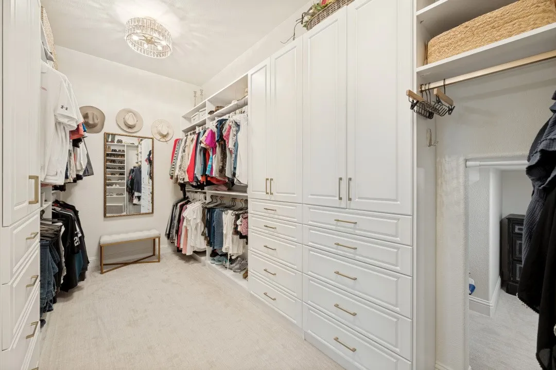 A spacious walk-in closet designed with both luxury and organization in mind, featuring a custom closet system with abundant built-in cabinetry, drawers, shelving, and generous hanging space. Soft, luxurious low-profile carpet adds warmth and comfort underfoot, creating a beautifully finished and highly functional dressing space. There's even a hidden storage space!