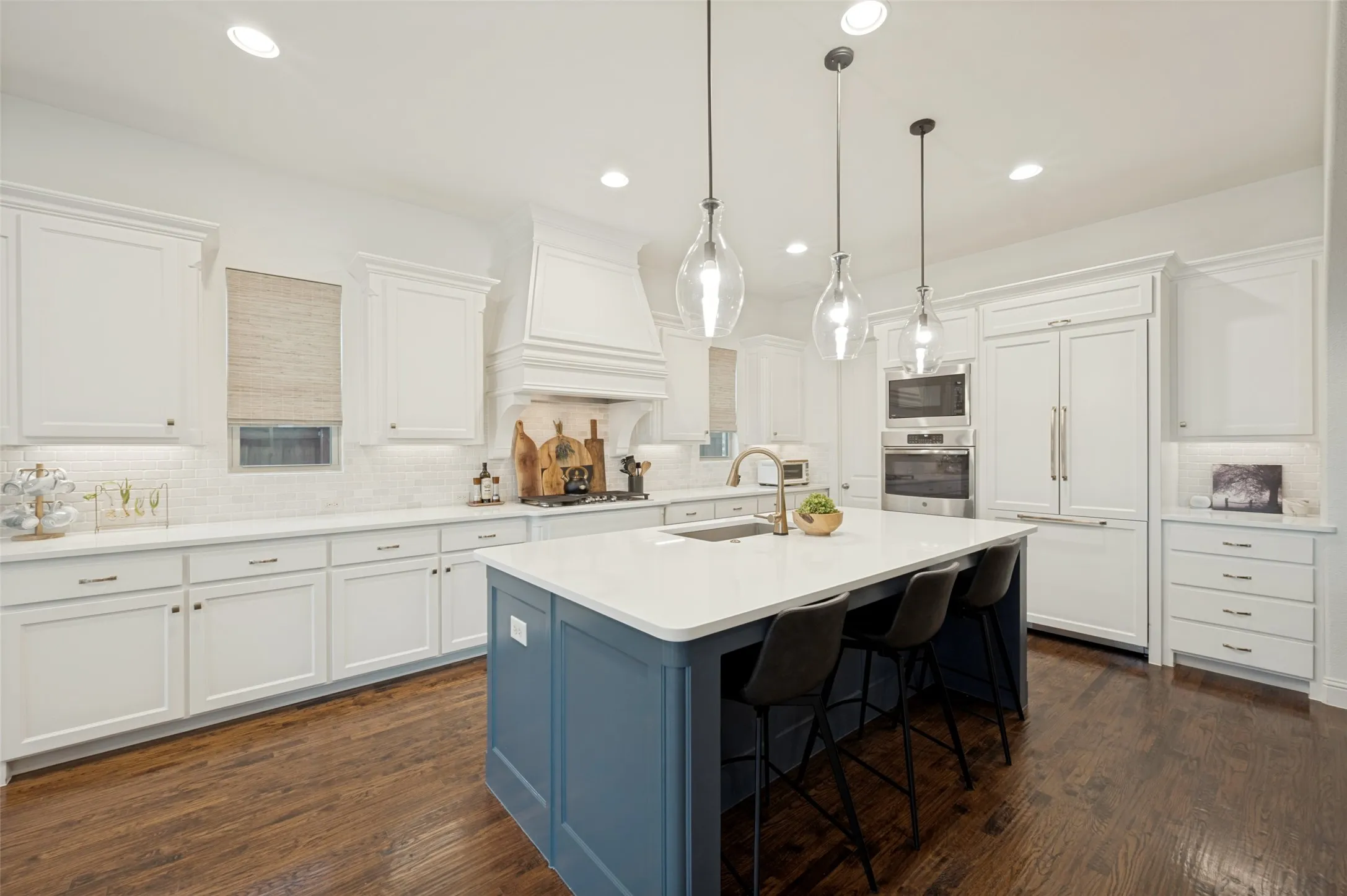 This well appointed kitchen offers both elegance and exceptional functionality, with a farmhouse sink, natural stone backsplash, and abundant custom cabinetry. Thoughtful details include hidden pull-out trash storage and a spacious walk-in pantry, while the oversized island provides generous prep space and seating for casual dining.